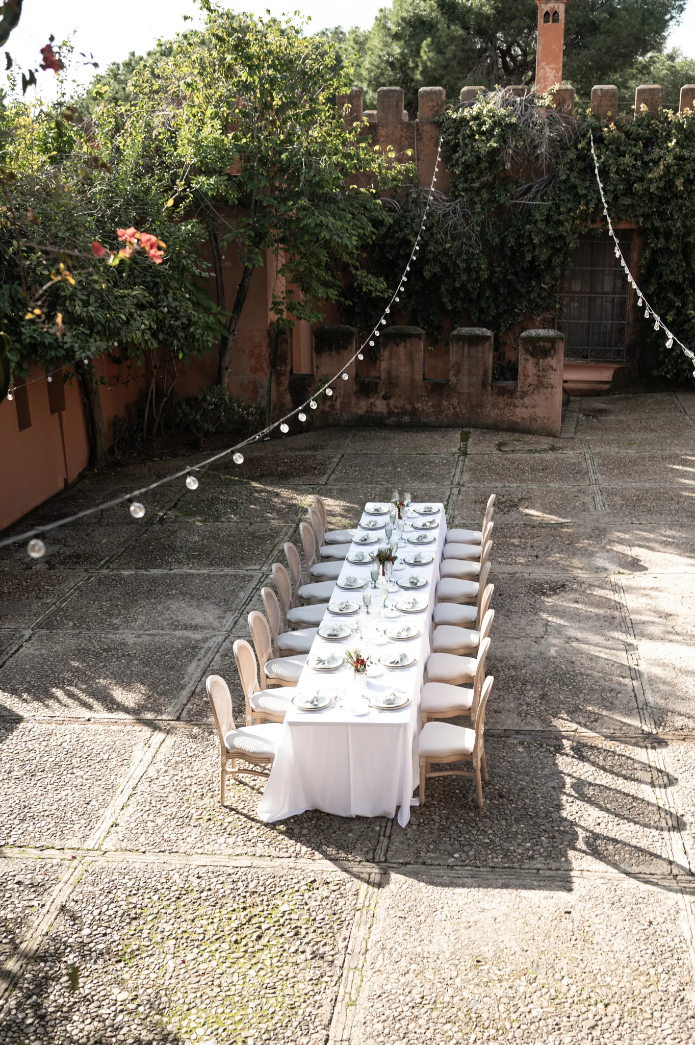 Mesa alargada para evento al aire libre con manteleria blanca y guirnaldas de luces